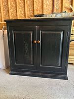 Front view of cabinet with doors closed showing distressed black finish and knobs