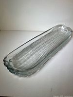 Two stacked elongated clear glass platters showing ribbed interior and scalloped end.