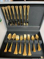 Open case showing gold flatware pieces arranged in slots