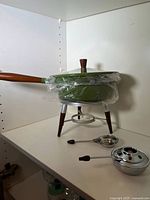 Full fondue set on shelf: pot with lid, stand, burner, forks