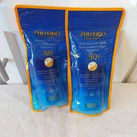 Front view of two sealed Shiseido SPF 50+ clear sunscreen sticks in retail pouches