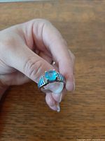 Hand holding sterling silver ring front view showing center blue topaz and opal inlays