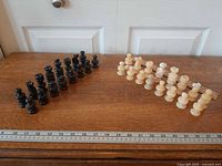 Full set of black and cream marble chess pieces arranged on table with ruler for scale