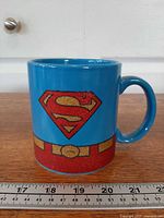 Full view of mug showing Superman logo and belt graphic with ruler for scale