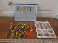Pegboard, pile of multicolour pegs, idea sheet placed on wooden surface with ruler for scale