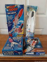 Group shot of all boxed items: Air Hogs Triple Booster, two Cosmic Rocket kits (front and back shown), packaged foam glider