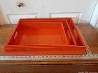 Top view of three nested orange trays beside ruler