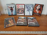 All seven DVD cases laid out on surface with ruler for scale