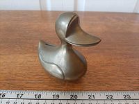Front-left view of brass duck coin bank with ruler for scale