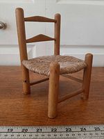 Front view of miniature wooden ladder-back chair with woven seat; ruler for scale