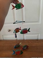 Full view of mobile held by hand showing top fish, crossbar, lower fish, additional fish pieces