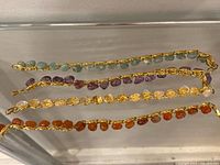 All four gold-tone chain bracelets laid flat showing stone colours and chain style