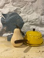 Group shot of fish sculpture, ceramic pear, yellow saucepan with underplate