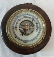 Front view of round wood-cased barometer showing porcelain dial and brass bezel