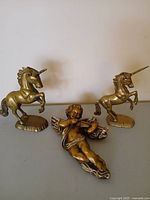 Group shot of two brass unicorn figurines and gold chalkware cherub plaque