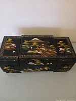 Top view of closed black lacquer jewelry box showing hand-painted landscape