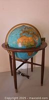 Full view of illuminated globe on three-leg wooden stand, power cord visible