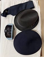 All four items displayed: navy tie, grey fedora, navy hat, goggles
