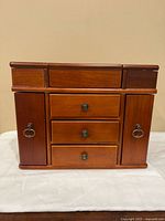 Front view of closed wooden jewellery box showing drawers and side doors