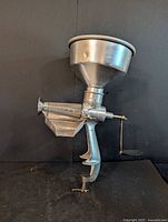 Full view of metal hand-crank strainer juicer showing funnel, crank, clamp base
