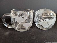 Creamer jug and sugar bowl with lid, showing etched globe design
