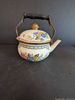 Front view of white enamel kettle with floral design, lid on, handle upright