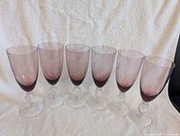 Six purple wine glasses lined up on cloth backdrop