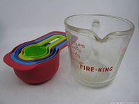 Glass Fire-King measuring cup beside nested plastic cups