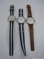 Front view of three Daniel Wellington wristwatches showing dial designs and straps