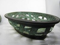 Side view of oval woven copper basket showing lattice pattern and verdigris patina