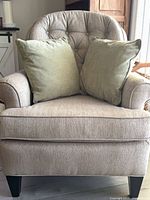 Front view of taupe upholstered accent chair with two green throw pillows