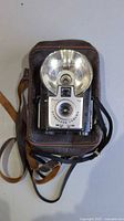 Full view of Kodak Brownie Starflash camera inside brown case with strap visible