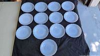 Fourteen blue opal glass saucers laid out showing quantity and overall condition