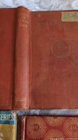 Front board and spine of Through the Looking Glass showing red cloth and gilt monogram