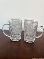 Four clear patterned glass beer mugs angled view
