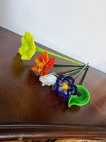 Five blown glass flower stems on wooden surface