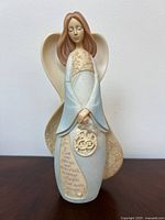 Front view of angel figurine showing gown, medallion and inscription