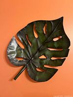 Full view of green metal palm leaf wall art against orange background