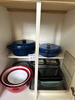 Cabinet showing full lot: two blue enameled cookware pieces, nested mixing bowls, loaf pans, baking dishes, cooling rack