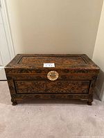 Front view of carved wood chest showing brass medallion and carved motifs