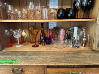 Overview of shelf with mixed painted stemware, decanter set, vases, tumbler, paperweight and clear bowl