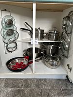 Overview of cabinet with stainless pots, pans, red silicone protectors and lid racks