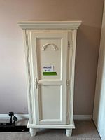Front view of tall white cabinet showing door, pull, feet and trim