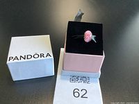 Charm displayed on ribbon in jewellery box lid showing pink glass and flower design