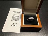 Ring in open display box beside lot card showing three-stone setting