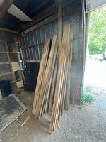 Stack of weathered barn boards leaning against wall showing quantity and condition