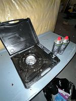 Stove open in carry case next to two fuel cans