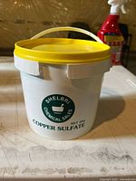 Front of white bucket with yellow lid showing Shelbri Chemical Sales Copper Sulfate label