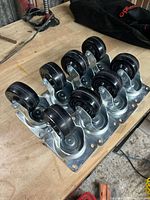 Eight caster wheels arranged on bench showing metal brackets and black rubber wheels