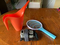 Group shot showing orange watering can, turquoise electric fly swatter, camo trail camera